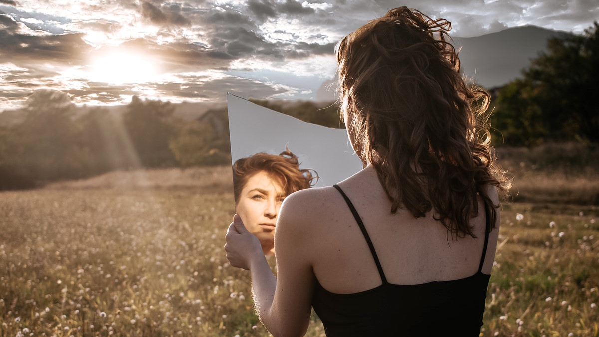 Девушка смотрит в зеркало на фоне природы