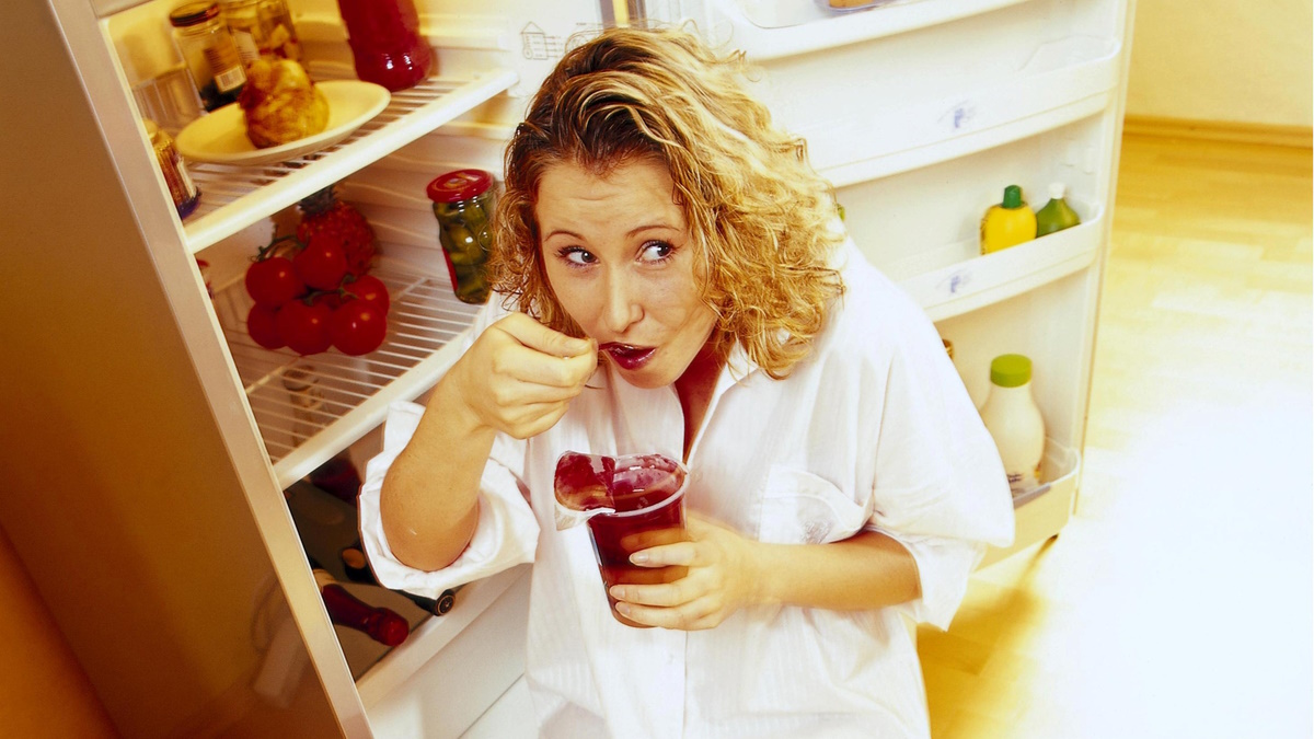 Женщина ест у холодильника