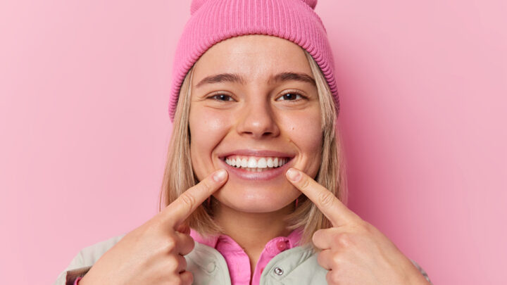 Девушка двумя руками показывает на свои белоснежные зубы