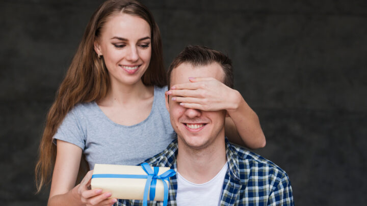 Девушка дарит подарок мужчине закрывая глаза рукой