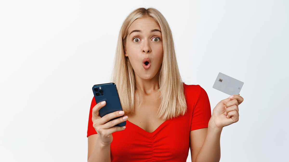 Удивленная девушка с телефоном и банковской картой в руках
