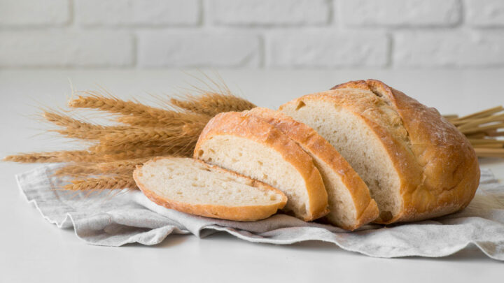 Хлеб нарезанный на кусочки лежит на полотенце, на столе. На заднем фоне колоски пшеницы