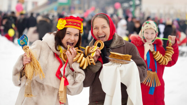 Две женщины в старо-русских наряд кусают баранки и улыбаются
