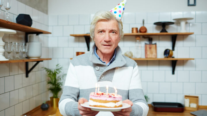 Мужчина с тортом со свечками в руках стоит на кухне