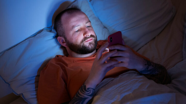 Мужчина лежит в кровати и смотрит в телефон