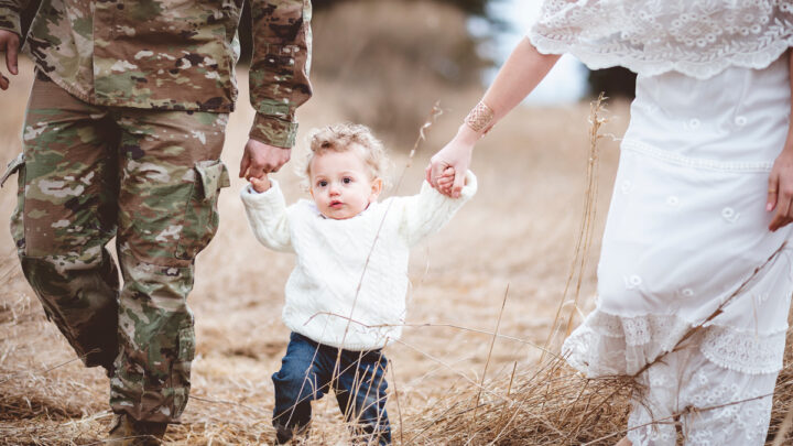 Отец-солдат с женой держат сына за руки с обеих сторон и гуляют по полю