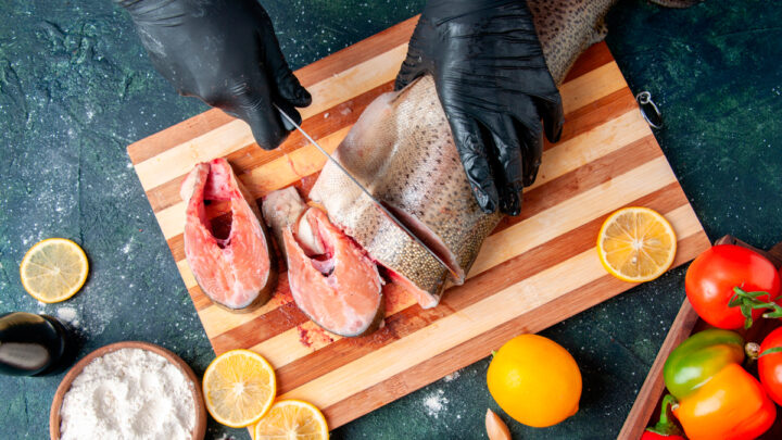 Повар, режущий сырую рыбу на разделочной доске, миска для муки, семена граната