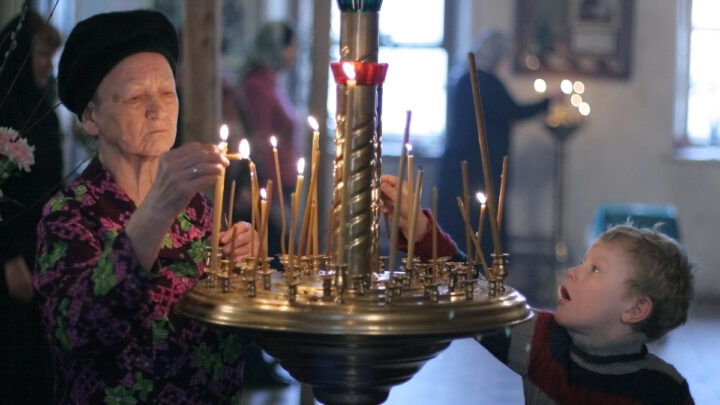 Бабушка и мальчик ставят свечи в церкви