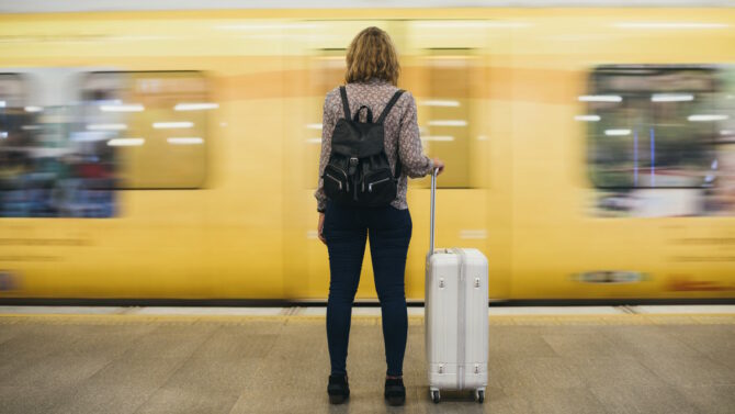 Девушка с чемоданом на фоне проезжающего поезда