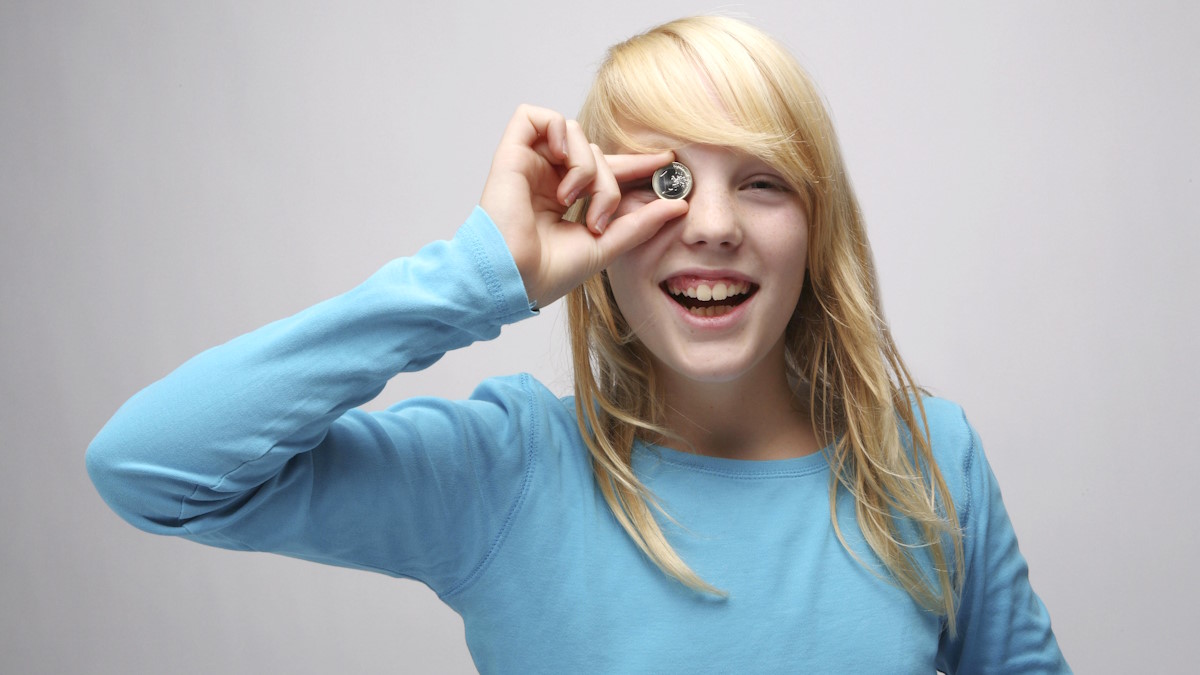 Девочка держит монету около глаза