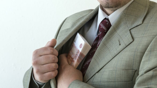 Мужчина прячет пачку денег в карман пиджака