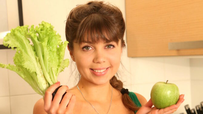 Девушка держит яблоко и лист салата в разных руках