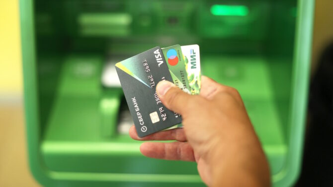 Рука держит кредитные карты на фоне банкомата