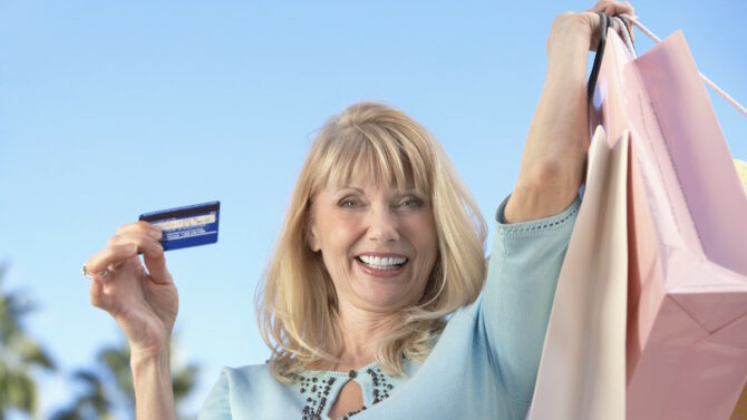 Счастливая женщина с пакетами в одной руке и кредиткой в другой
