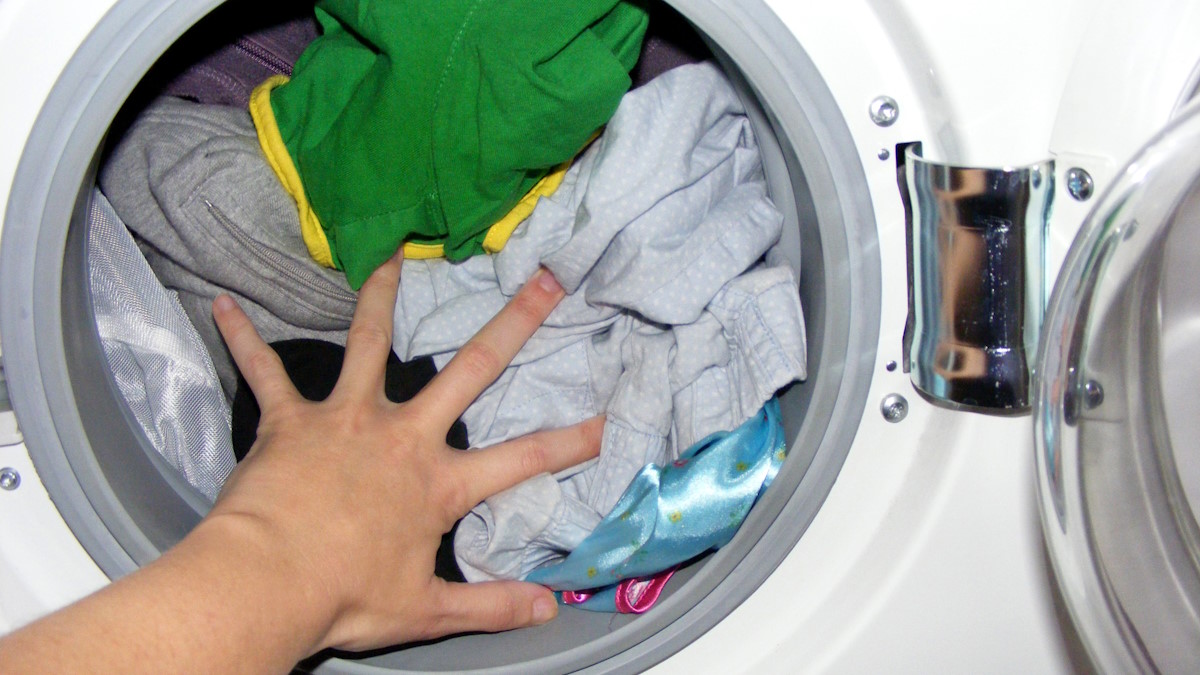 Рука прижимает белье в барабане стиральной машинки