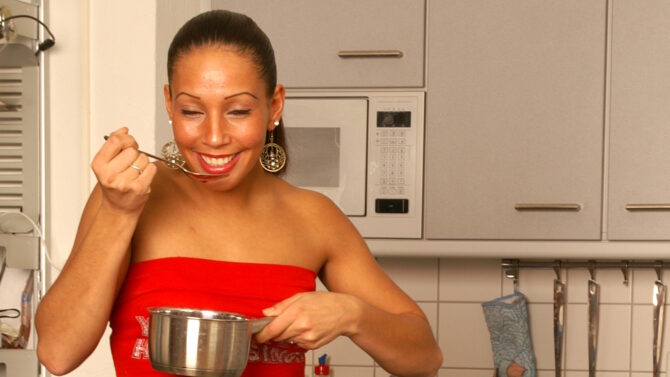 Женщина на кухне держит ложку у рта