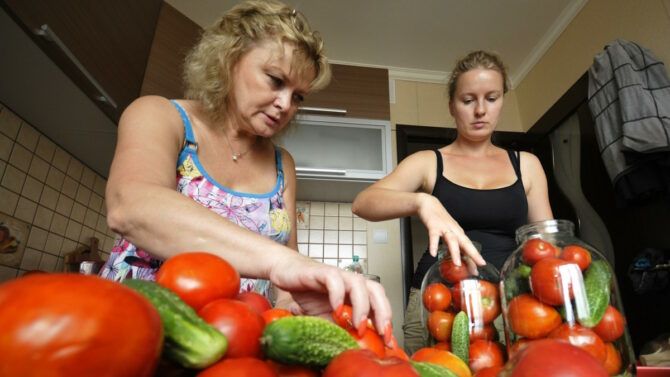 Две женщины консервируют помидоры и огурцы