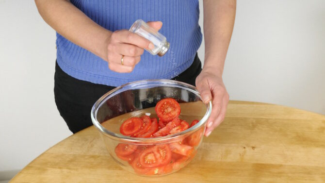 Женщина солит помидоры в салатнице
