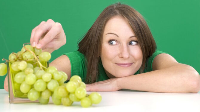 Женщина отщиаывает виноград от грозди