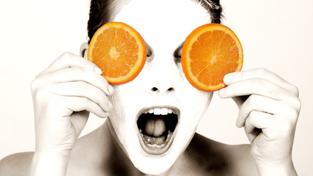 Девушка с косметической маской на лице закрывает глаза апельсиновыми дольками