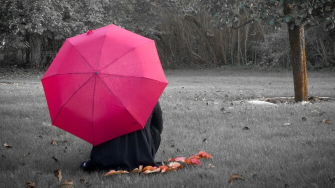 Девушка сидит в саду под зонтиком