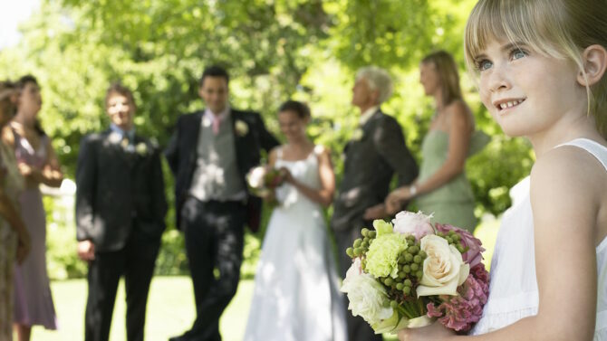Девочка с букетом цветов на фоне жениха и невесты